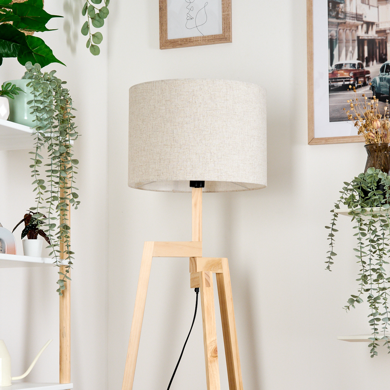 Hölzerne Stativ-Stehlampe mit Leinen-Lampenschirm, in einem Raum mit Pflanzen und Deko.