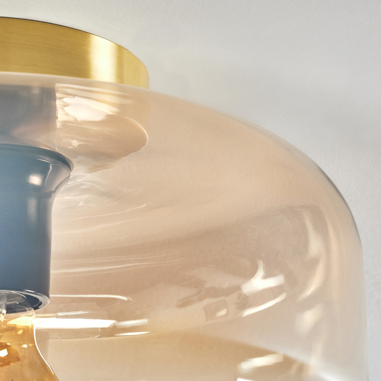 Nahaufnahme der orangefarbenen Glas-Deckenleuchte. Goldener Sockel und leuchtende Glühbirne. Innendetails.
