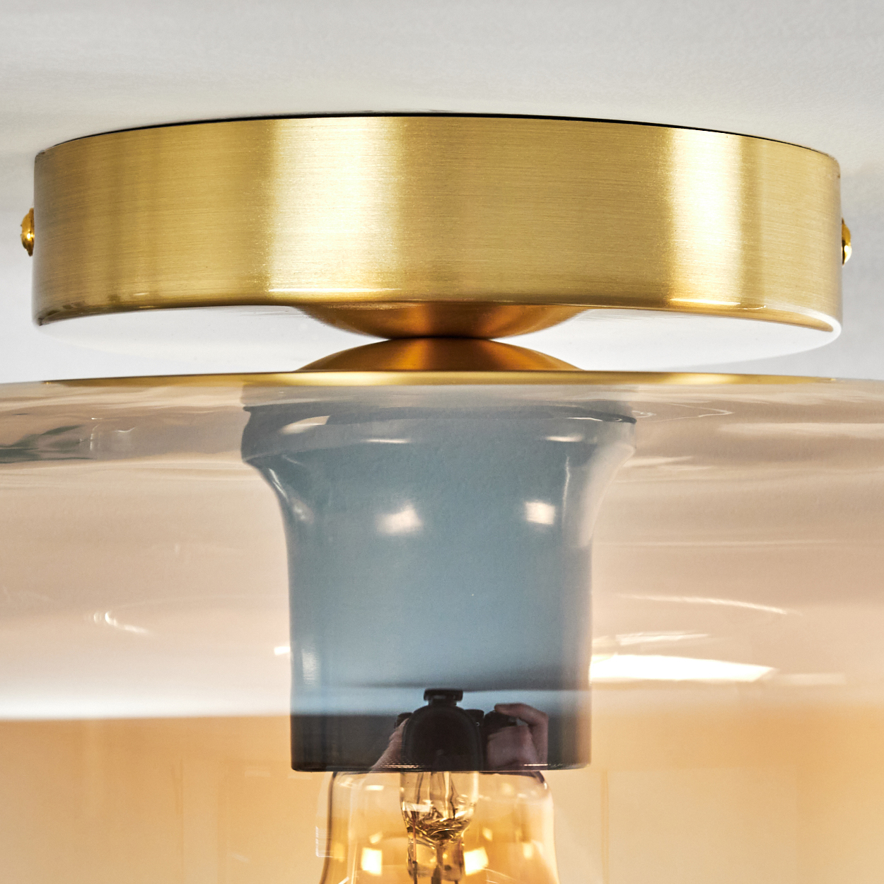 Nahaufnahme einer Deckenleuchte mit Glasschirm und goldenem Sockel.
