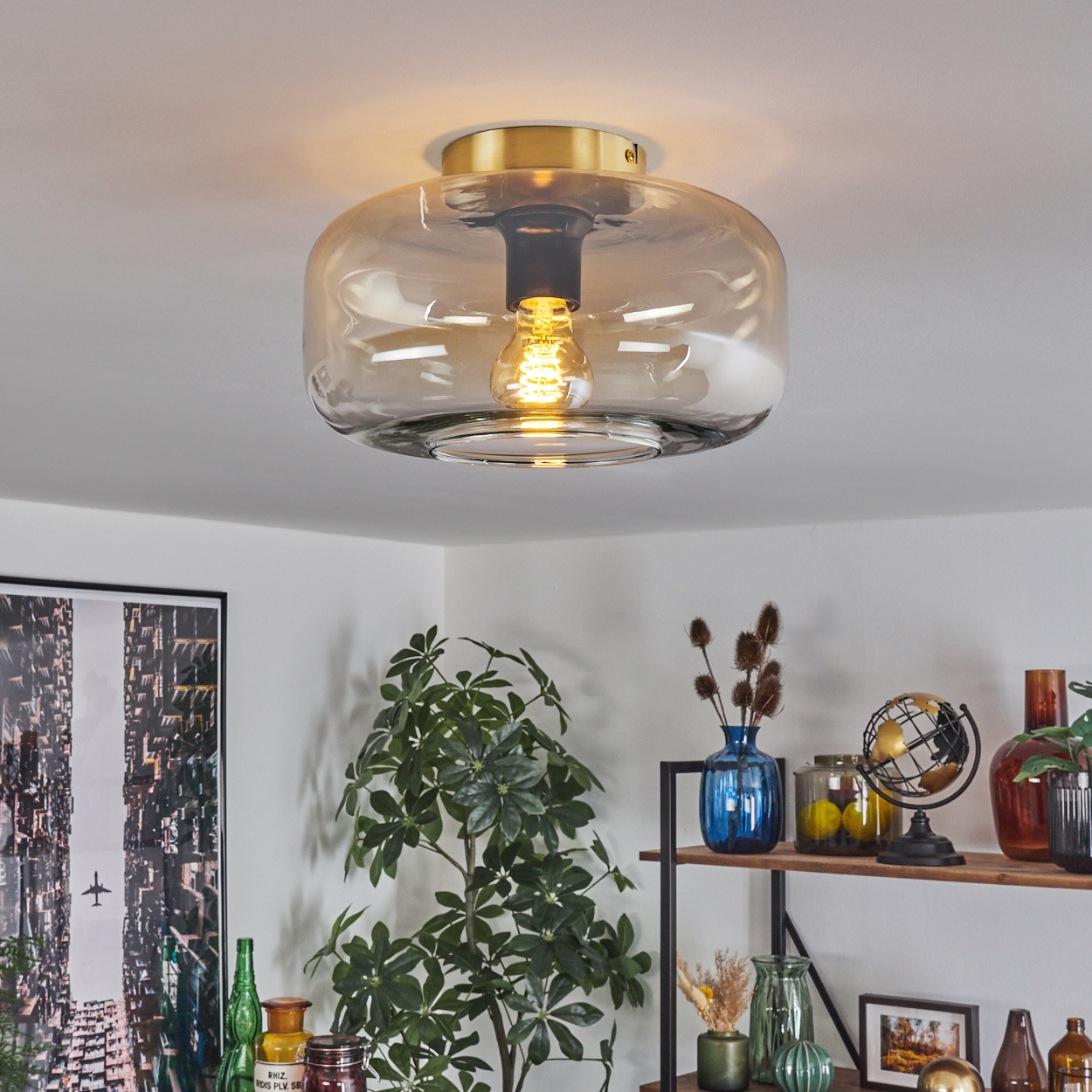 Runde Deckenleuchte aus bernsteinfarbenem Glas mit sichtbarer Glühbirne, montiert auf goldfarbenem Sockel, vor weißer Decke.
