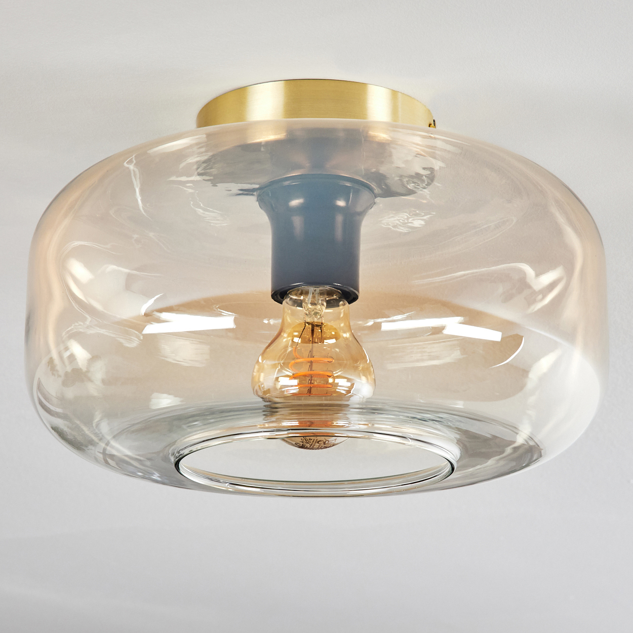 Eine Deckenleuchte mit Glasschirm und gelber Edison-Glühbirne. Die Decke und das Licht sind weiß.