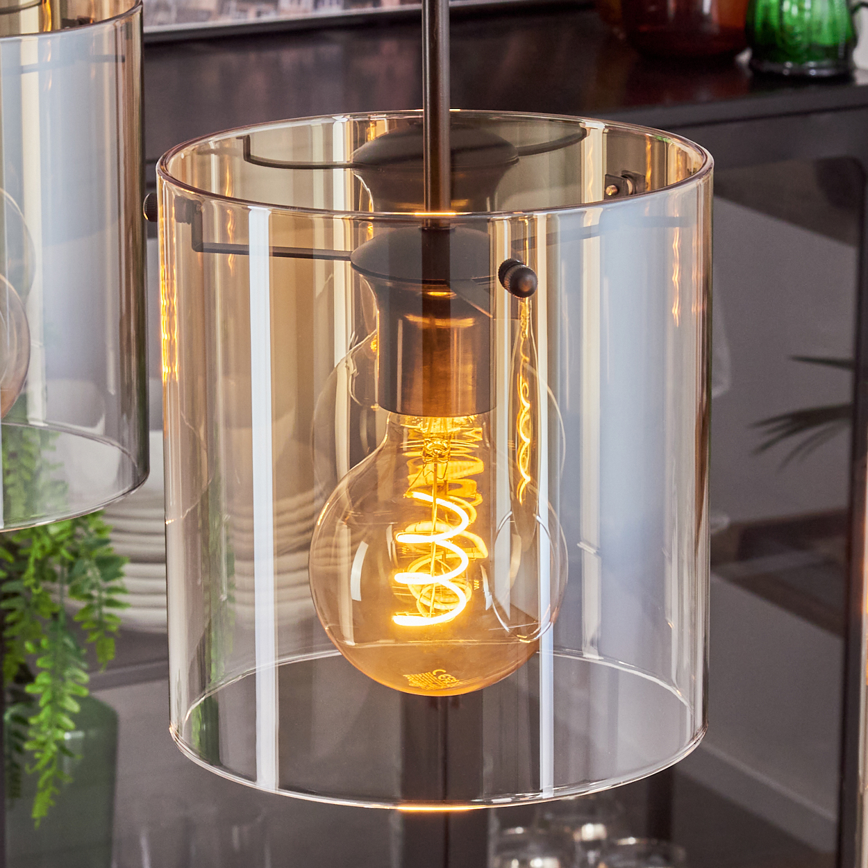 Nahaufnahme einer Pendelleuchte mit bernsteinfarbenem Glasschirm und Edison-Glühbirne.