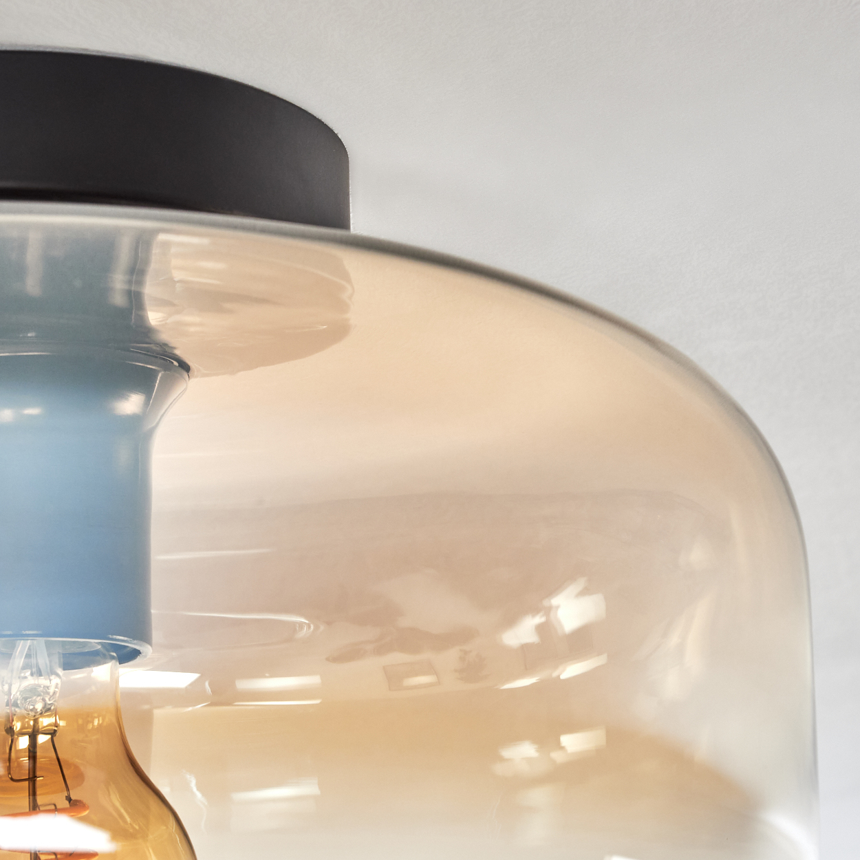 Nahaufnahme eines Glaslampenschirms mit bernsteinfarbener Farbe. Das Glas ist gebogen und transparent. Die Glühbirne ist sichtbar.
