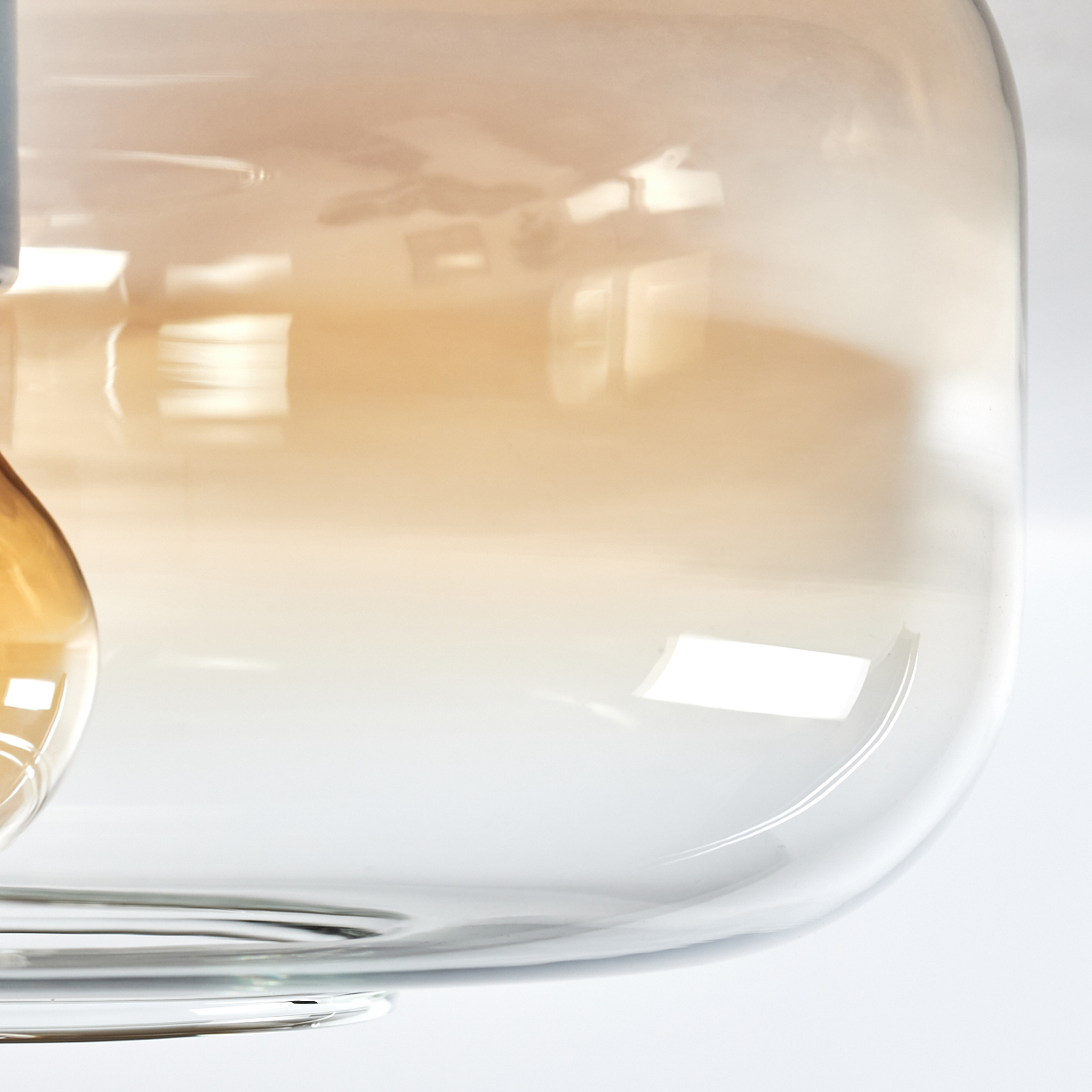 Nahaufnahme eines transparenten, gebogenen Glaslampenschirms mit Bernsteintönen. Das Glas hat eine glatte, reflektierende Oberfläche.