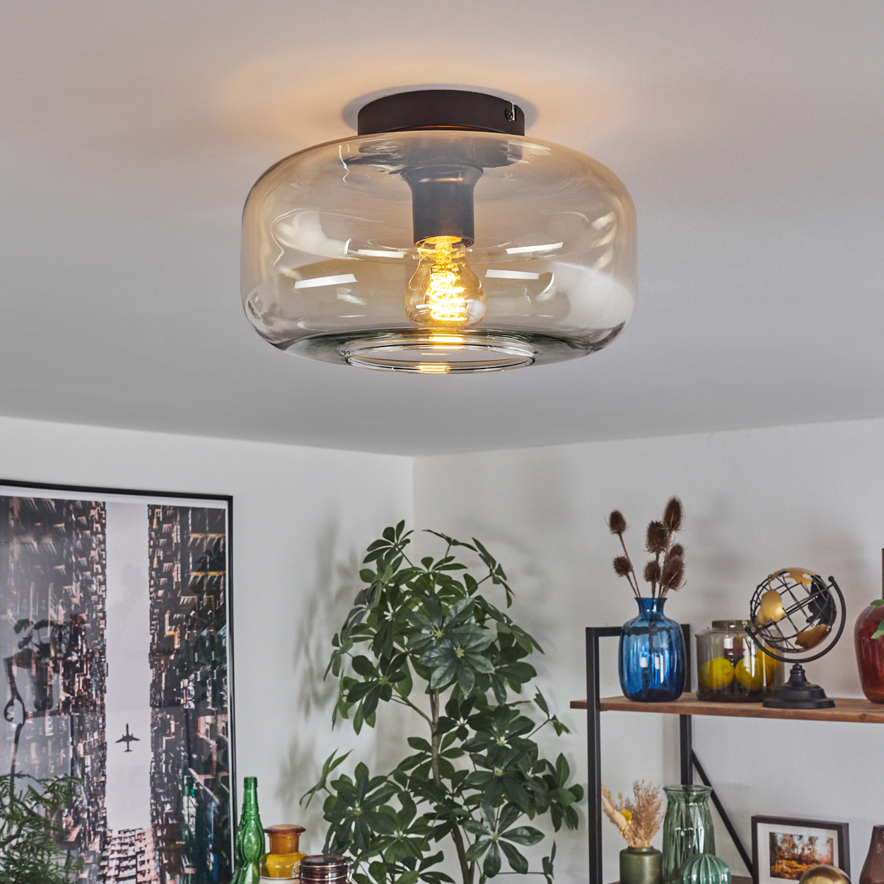 Deckenlampe mit Glasschirm über einem Raum mit Pflanzen, Büchern und Dekorobjekten. Warmes Licht.