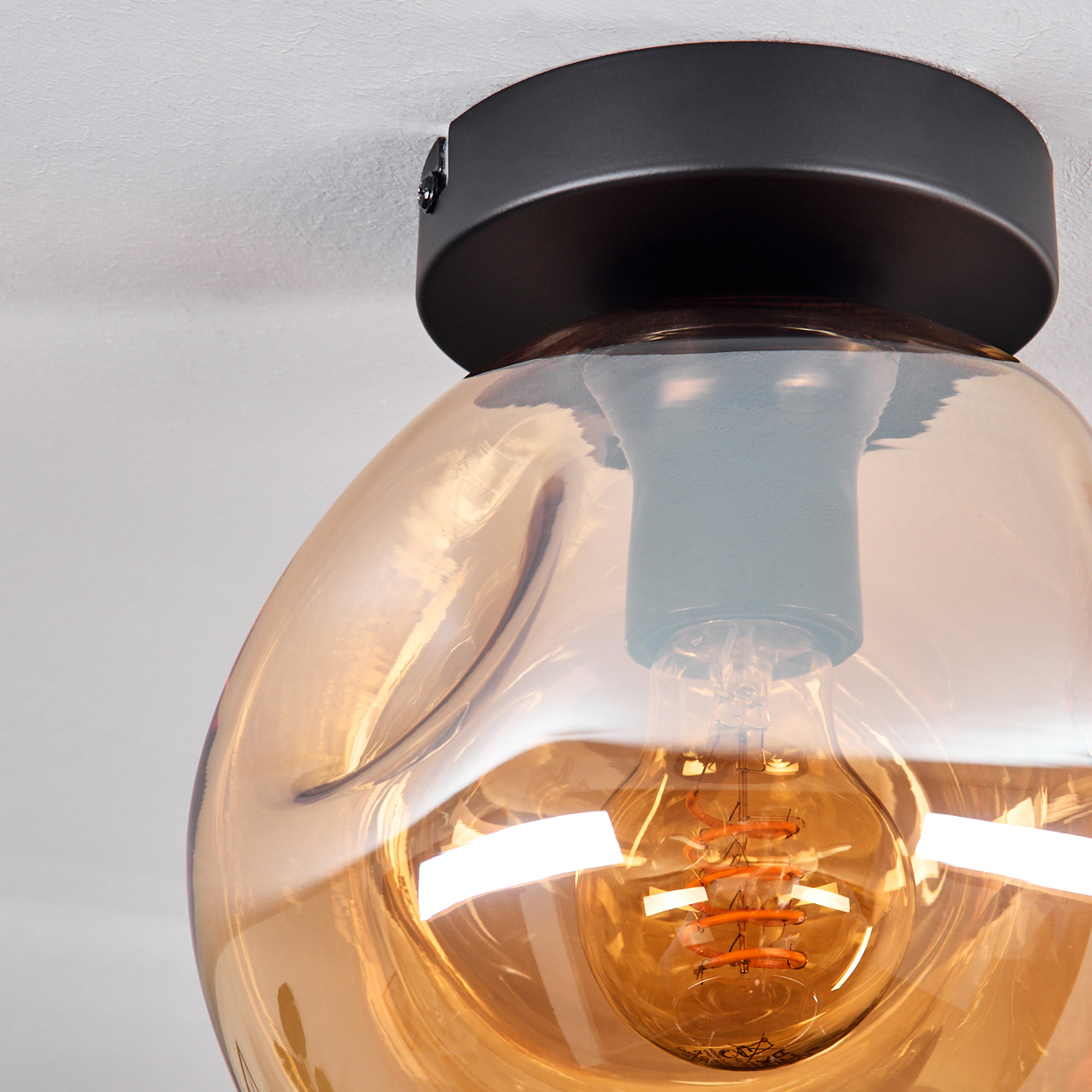 Nahaufnahme einer Deckenleuchte mit bernsteinfarbenem Glasschirm und einer leuchtenden Glühbirne. Die Lampe ist rund.
