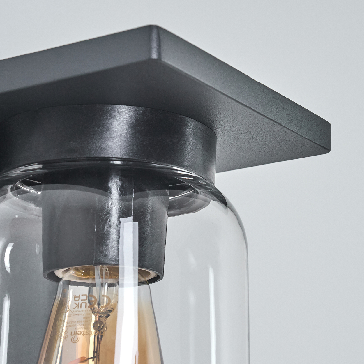 Nahaufnahme einer schwarzen quadratischen Wandleuchte mit Glas und Glühbirne.
