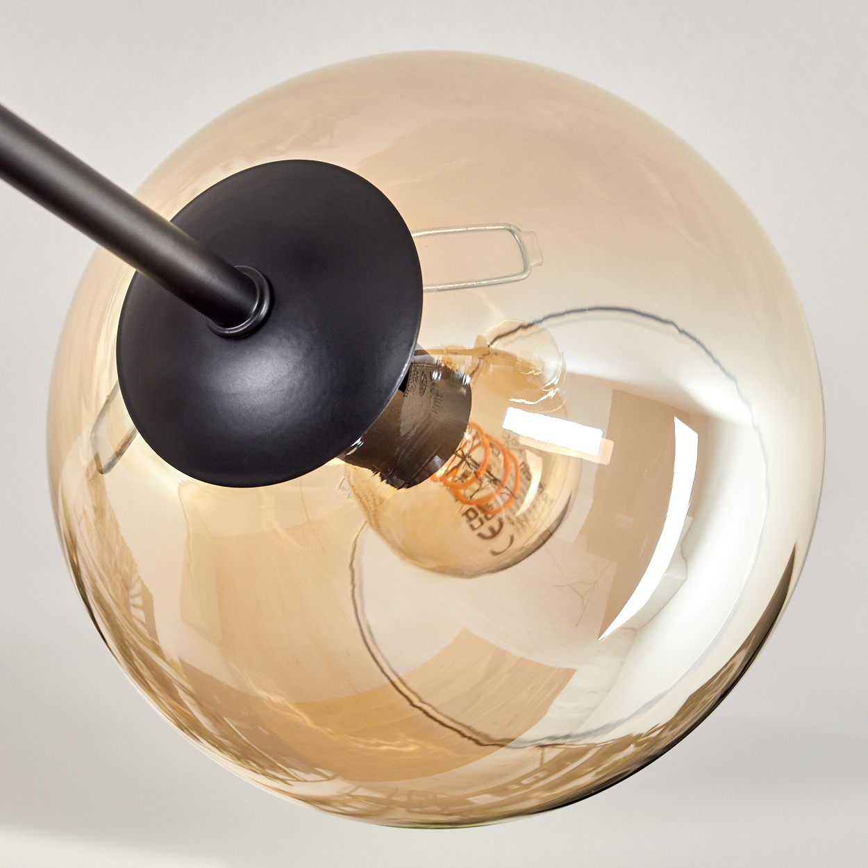 Nahaufnahme einer Glühbirne in einer bernsteinfarbenen Glaskugel. Das Glas ist reflektierend und transparent.