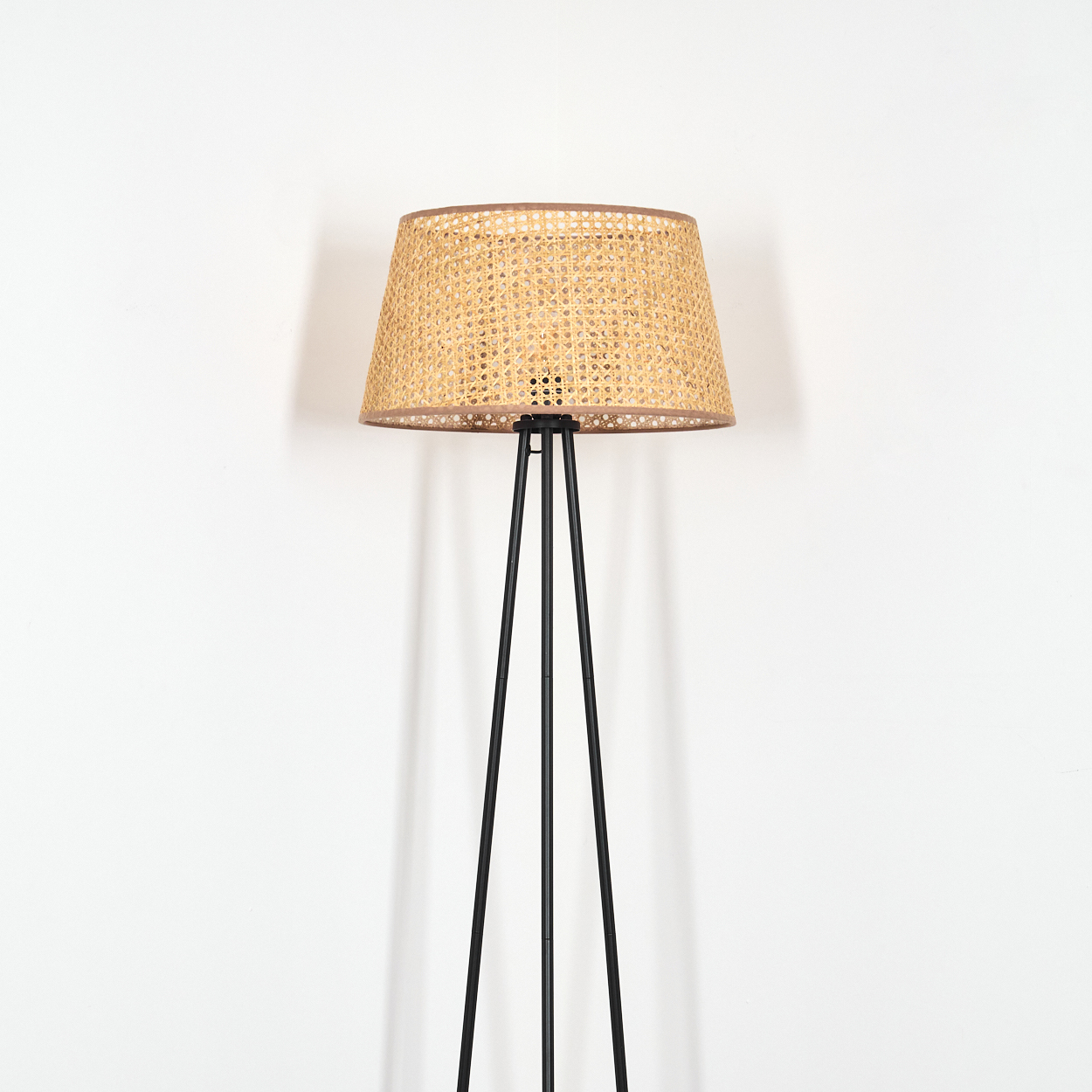 Stehlampe mit Rattanschatten und schwarzem Rahmen vor weißer Wand.