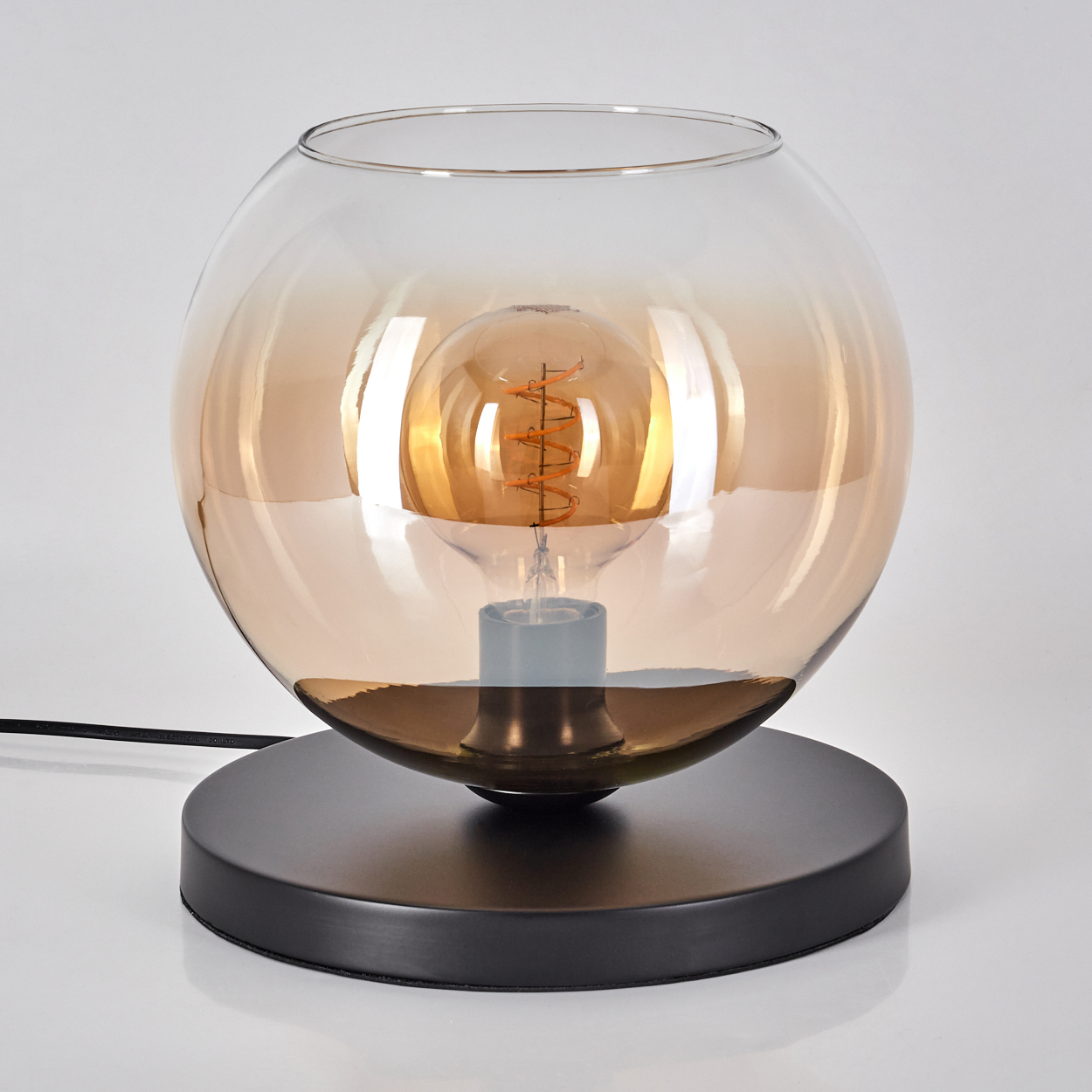 Eine Tischlampe mit braunem Glaskugel-Schirm und schwarzem Fuß, eine leuchtende Glühbirne innen.
