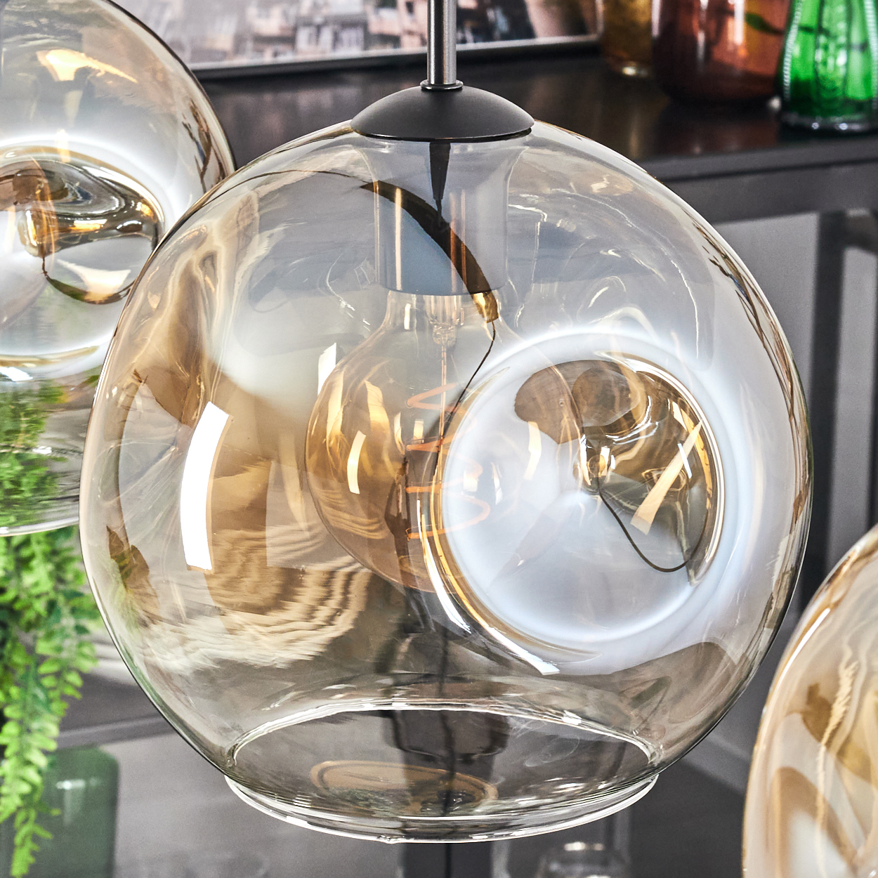 Nahaufnahme einer Glas-Pendelleuchte mit bernsteinfarbener Glühbirne. Licht kommt von der Glühbirne im Inneren.