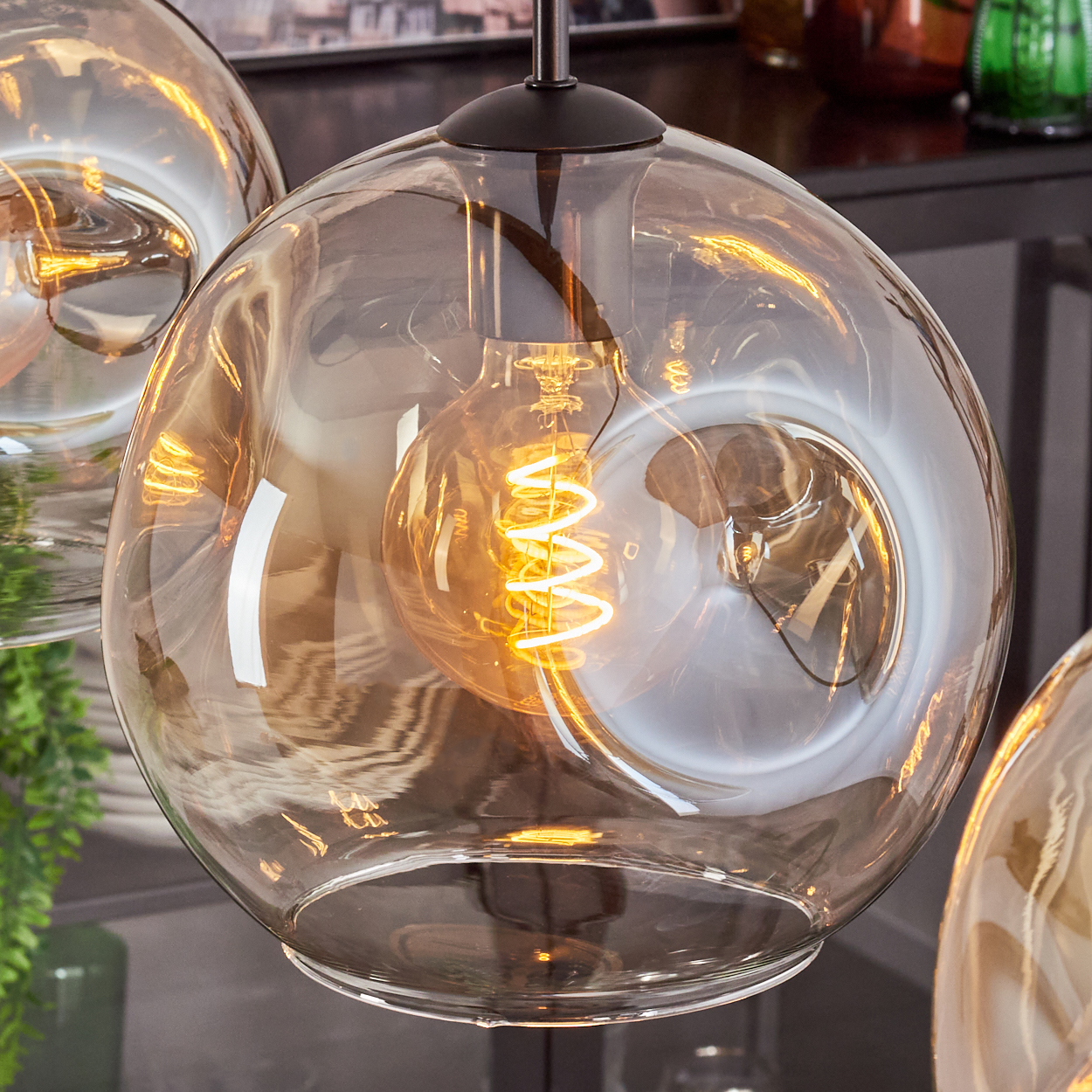 Nahaufnahme einer Glas-Pendelleuchte mit einer bernsteinfarbenen Glühbirne mit Wendelfaden. Das Glas ist klar.