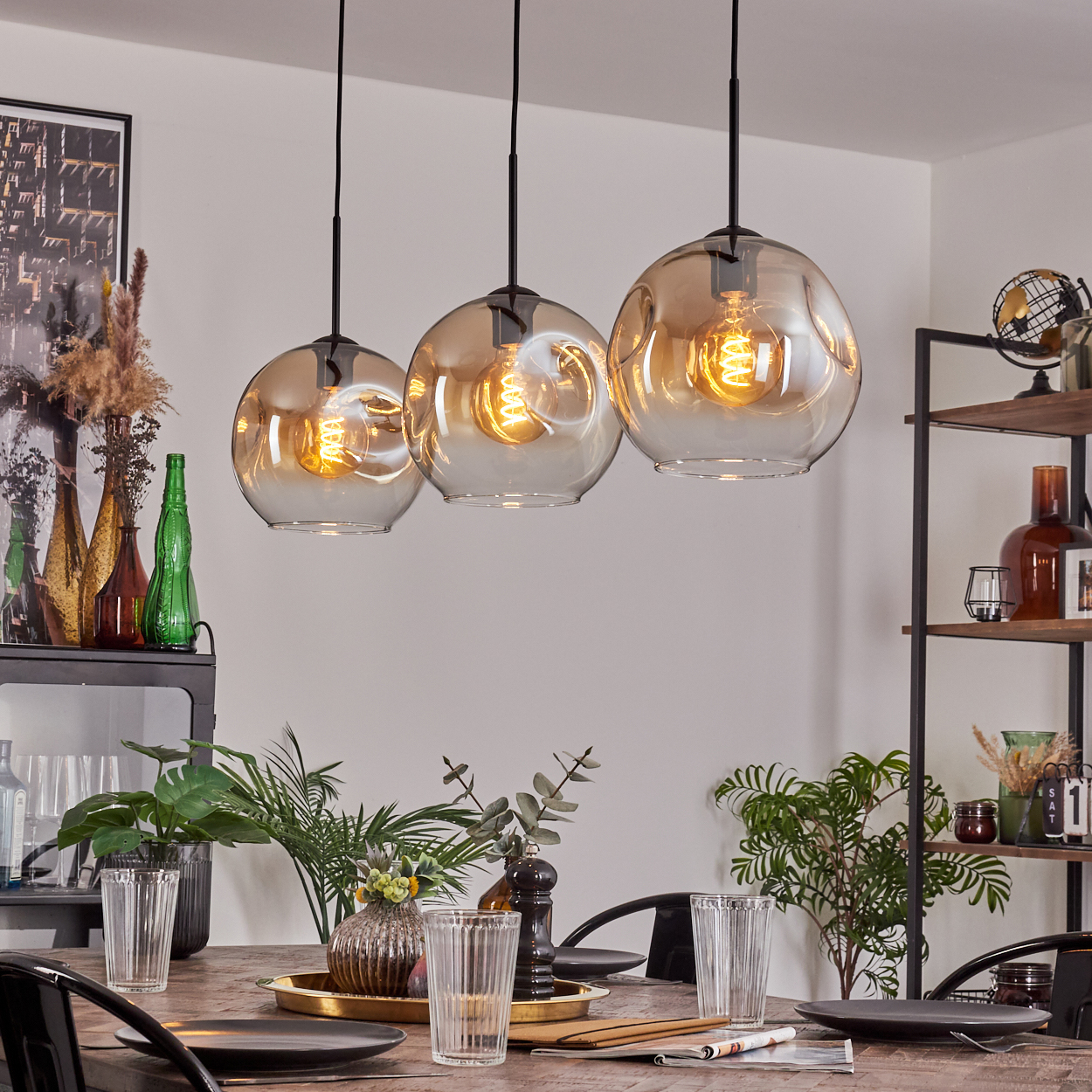 Ein Esszimmer mit drei Pendelleuchten über einem Tisch. Dekoriert mit Pflanzen und Kunst.