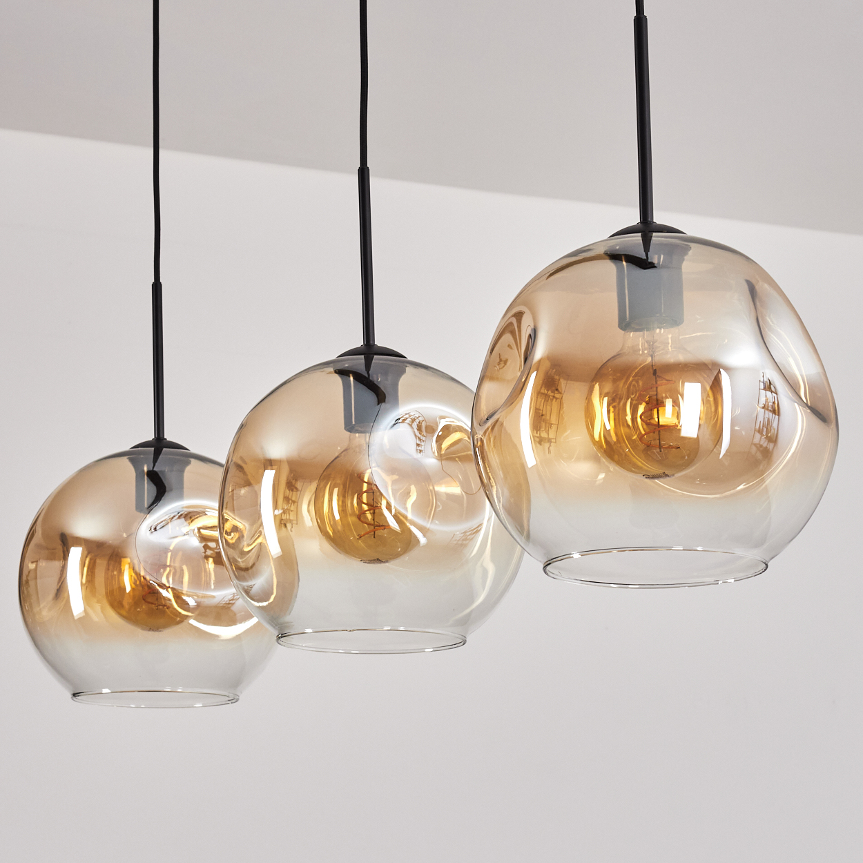 Drei hängende Glas-Pendelleuchten mit bernsteinfarbenen Glühbirnen.