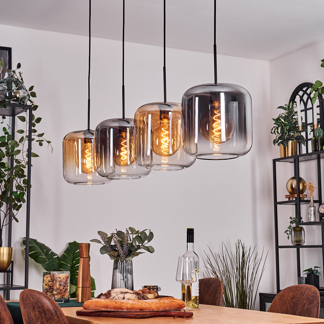 Esszimmer mit vier Pendelleuchten über einem Holztisch. Dekoriert mit Pflanzen.