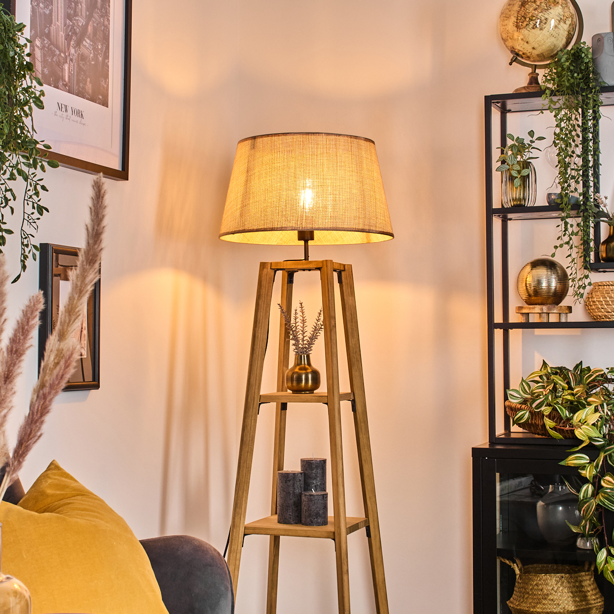 Stehlampe mit gewebtem Lampenschirm, Pflanzen und schwarzem Regal. Zusätzliche Dekoration sind Kerzen.