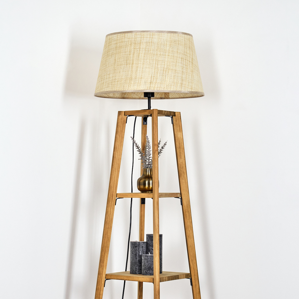 Eine Stehlampe mit beigem Lampenschirm, einer Vase und Kerzen. Der Hintergrund ist eine weiße Wand.
