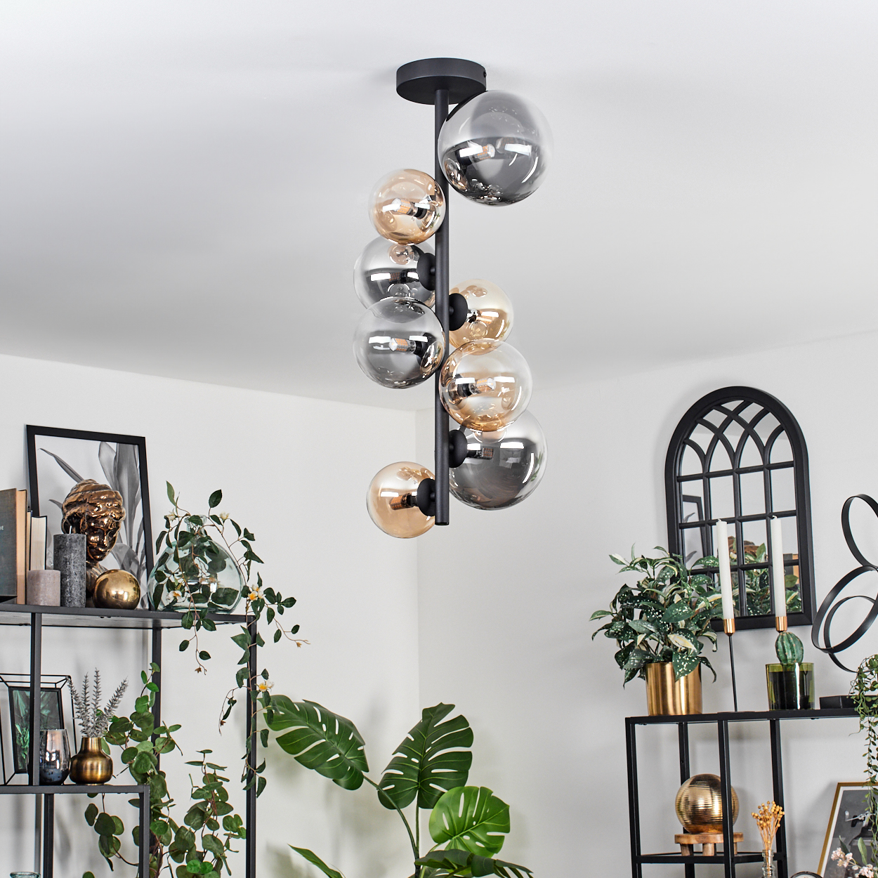 Eine schwarze Pendelleuchte mit mehreren Glaskugellampen hängt von der Decke in einem Raum mit Dekoration.