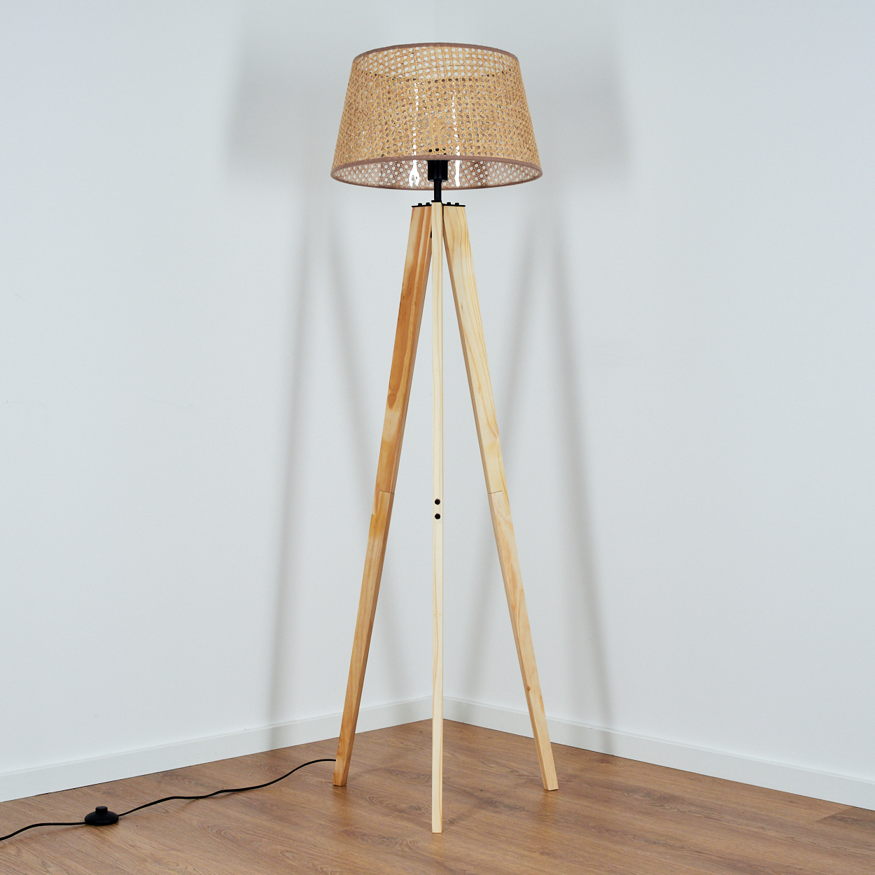 Hölzerne Stativ-Stehlampe in einer Ecke. Lampe leuchtet mit gewebtem Lampenschirm.