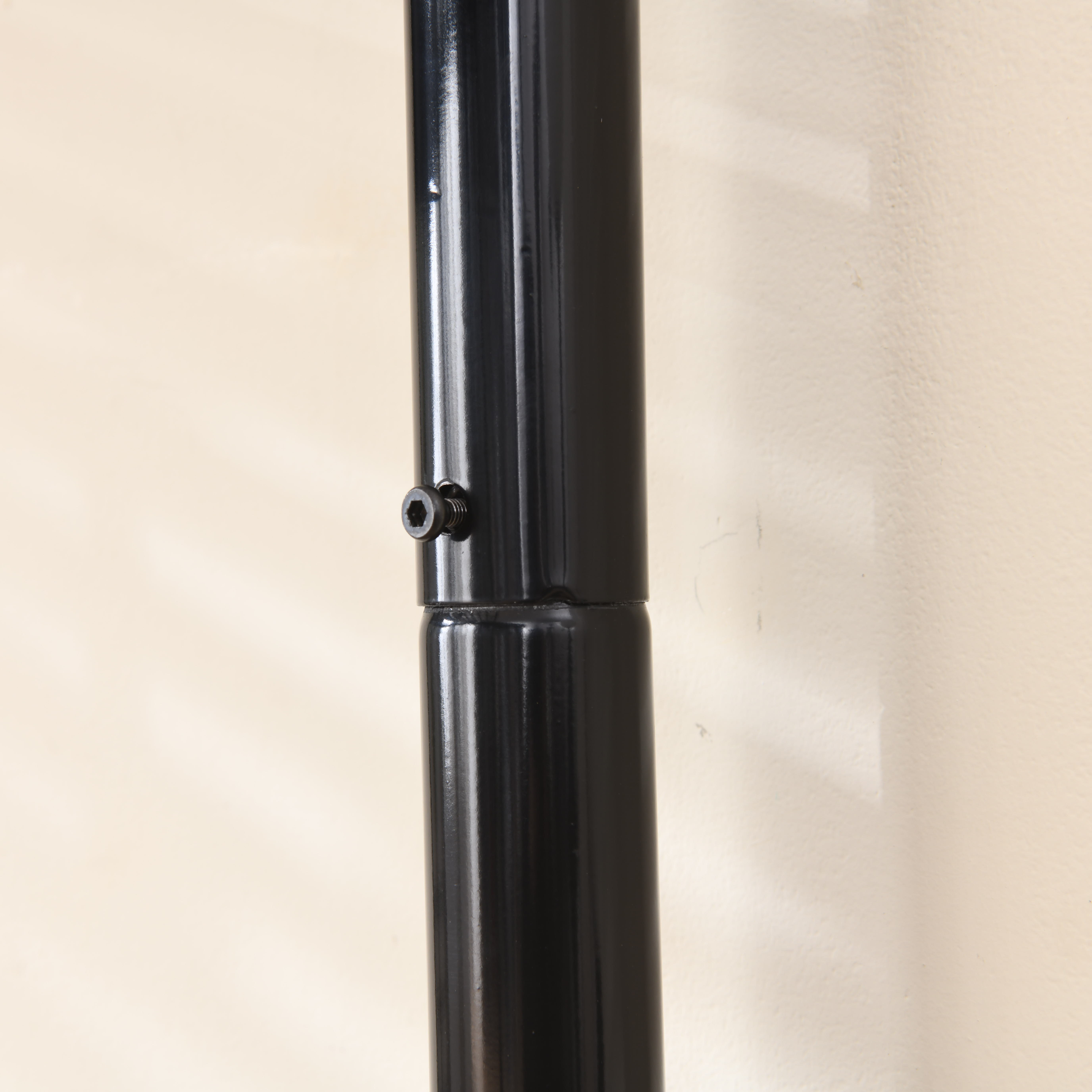 Nahaufnahme einer schwarzen Metallstange mit Schraubverbindung. Beige Wand im Hintergrund.