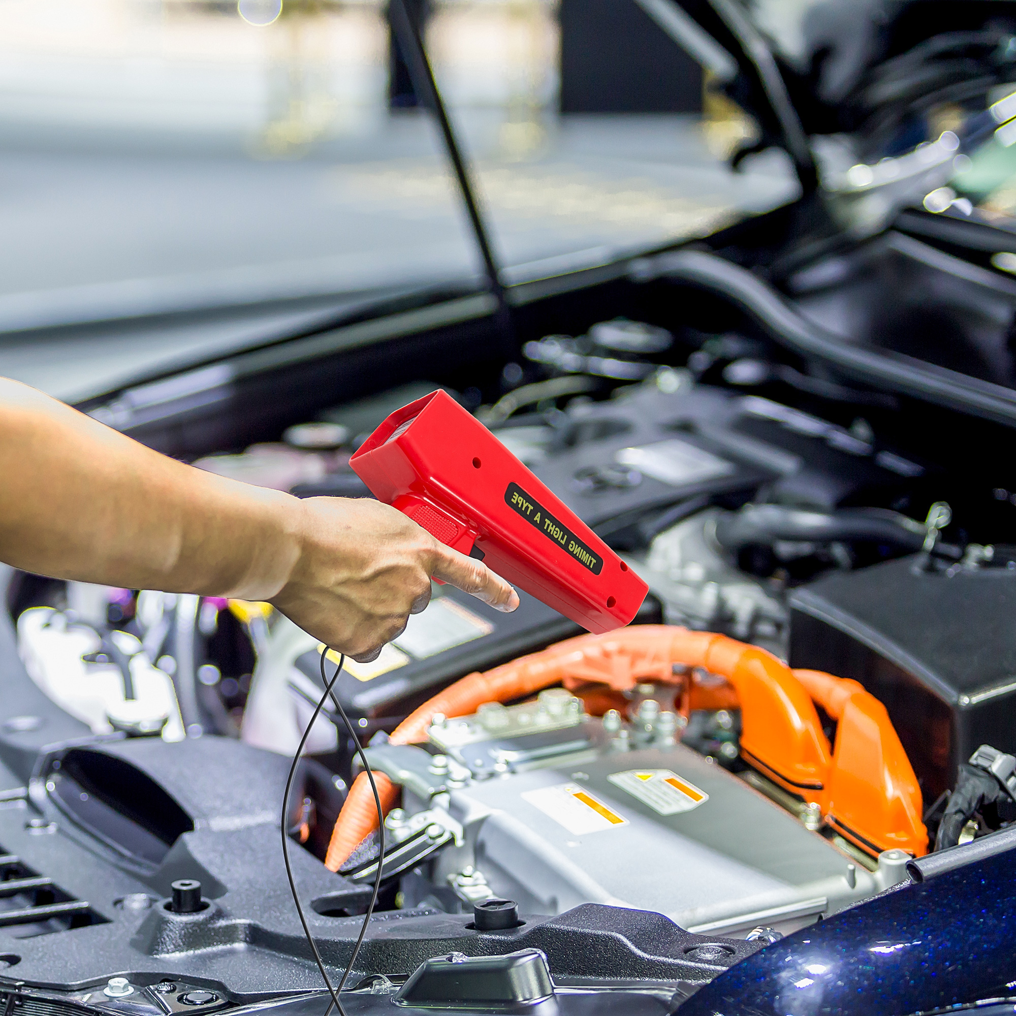 Eine Hand hält eine rote Blitzpistole in der Nähe eines Automotors und inspiziert dessen Komponenten.
