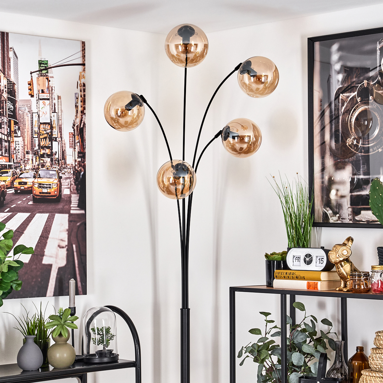 Zimmer mit Stehlampe mit fünf goldenen Kugeln. Enthält ein gerahmtes NYC-Bild, Regale mit Dekoration und Pflanzen.