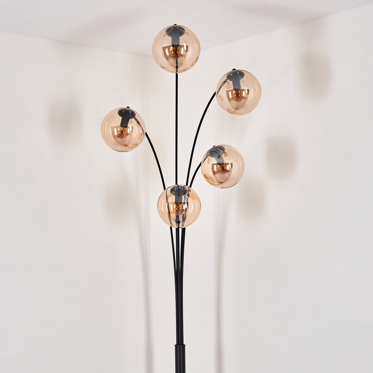 Schwarze Stehlampe mit fünf Kugelleuchten. Die Lampe steht in einer Ecke vor einer weißen Wand.