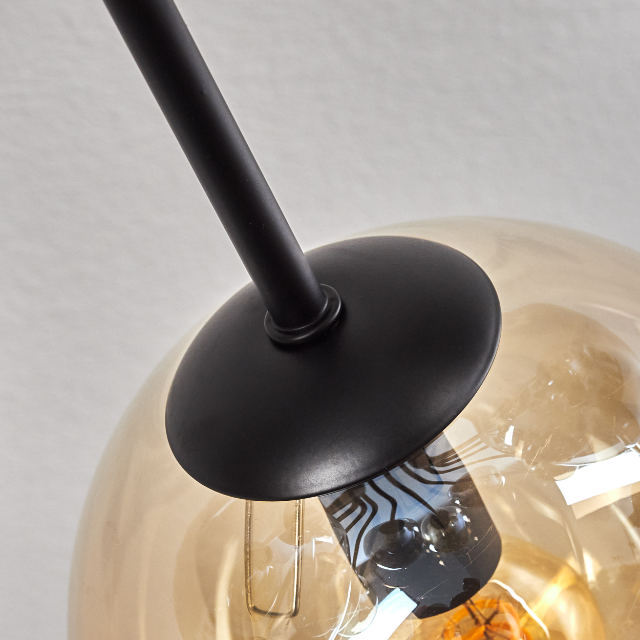 Nahaufnahme eines goldenen Globus auf einer schwarzen Lampe. Zeigt die Glühbirne und den schwarzen Stiel, der den Globus hält.