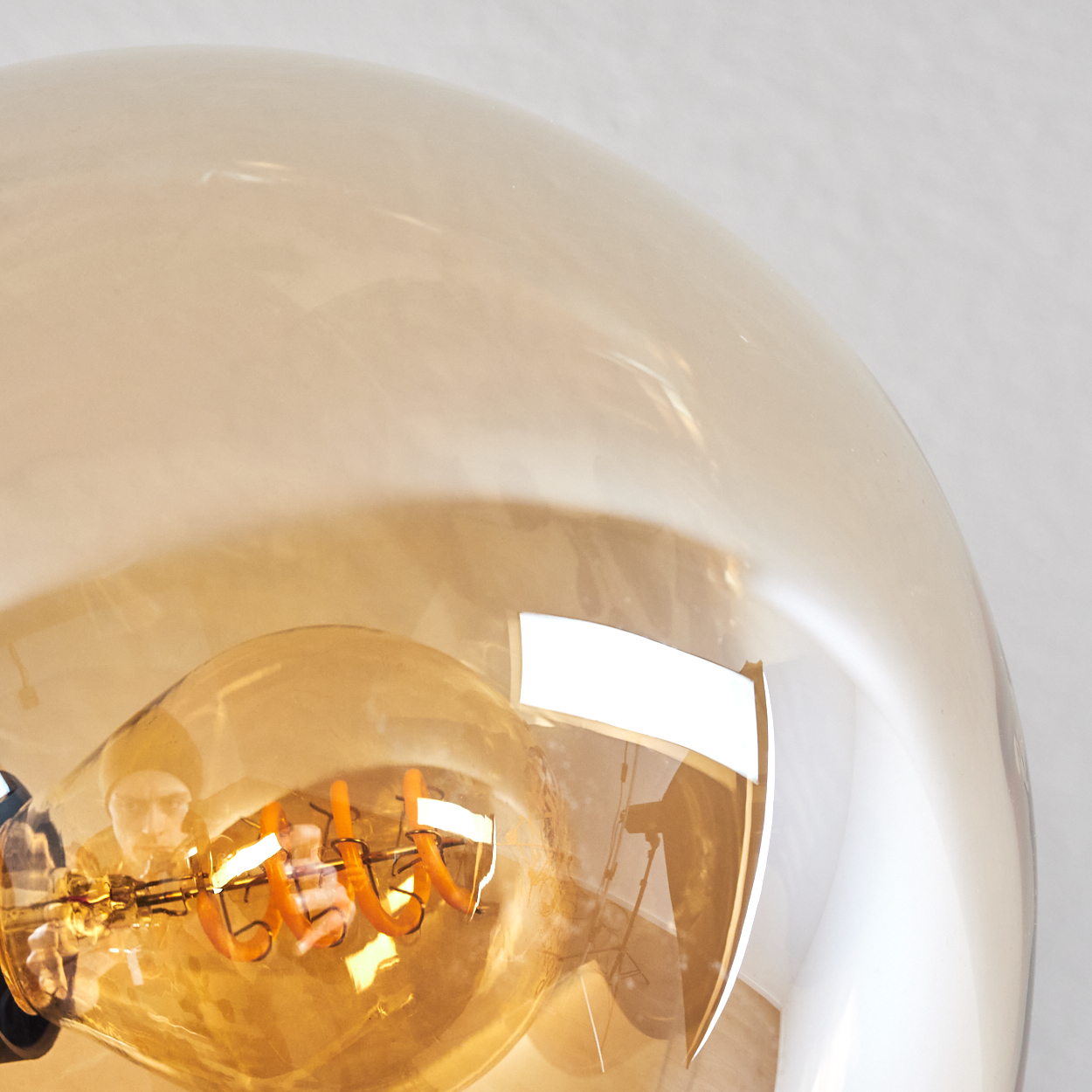 Nahaufnahme einer Glühbirne mit warmem orangefarbenem Glühfaden in einem durchsichtigen Glasschirm.