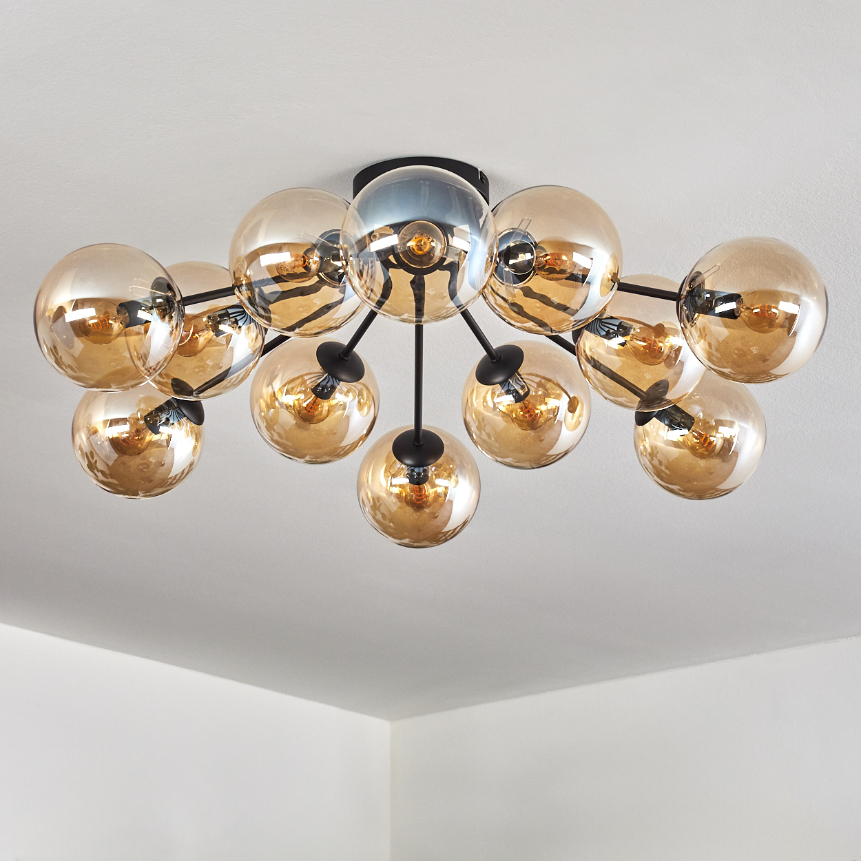 Deckenlampe mit goldenen Kugeln. Schwarze Stiele verbinden die Kugeln mit der Mitte. Weißer Hintergrund.