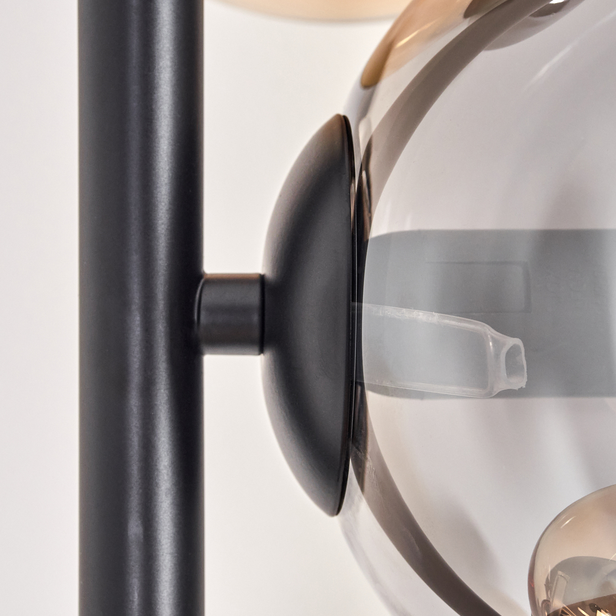 Nahaufnahme einer schwarzen Leuchte mit einem transparenten Glaskugelförmigen Leuchtkörper, die das Befestigungsdetail zeigt.