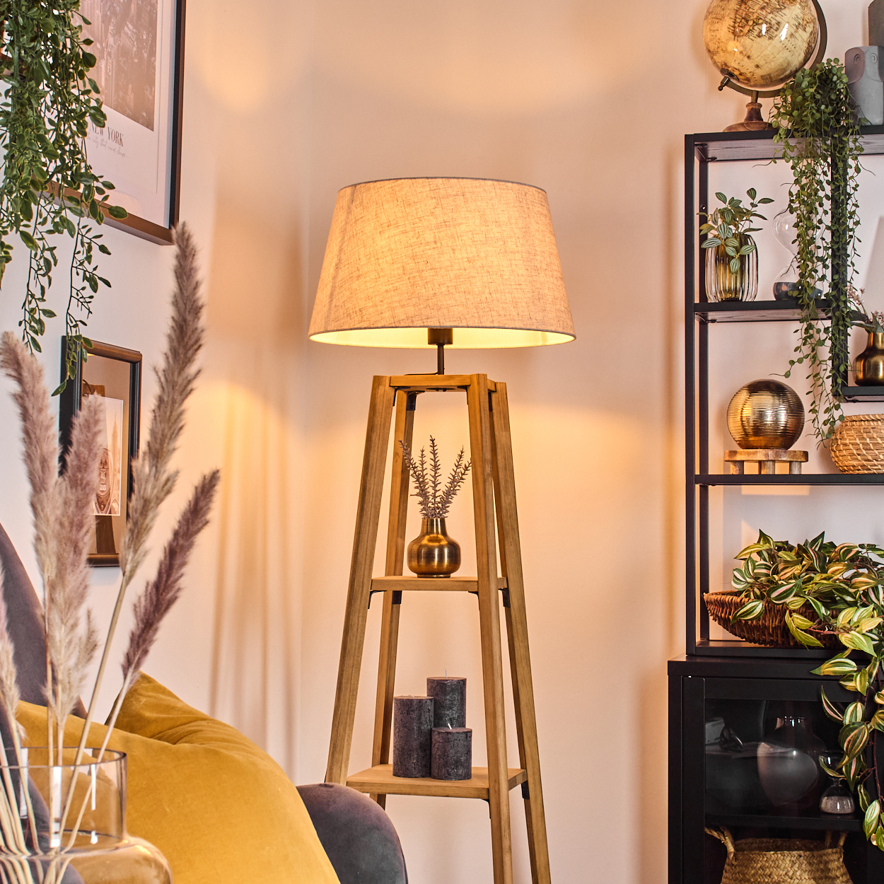 Stehlampe in einem Raum. Sie hat einen beigen Lampenschirm, zwei Regale, eine Vase und Kerzen. Dekorationen im Hintergrund.