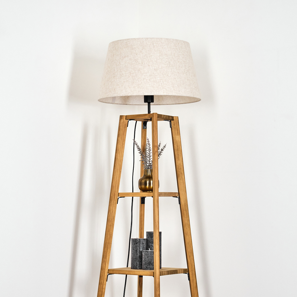 Holz-Stehlampe mit beigem Lampenschirm. Vase mit Pflanze auf Regal.