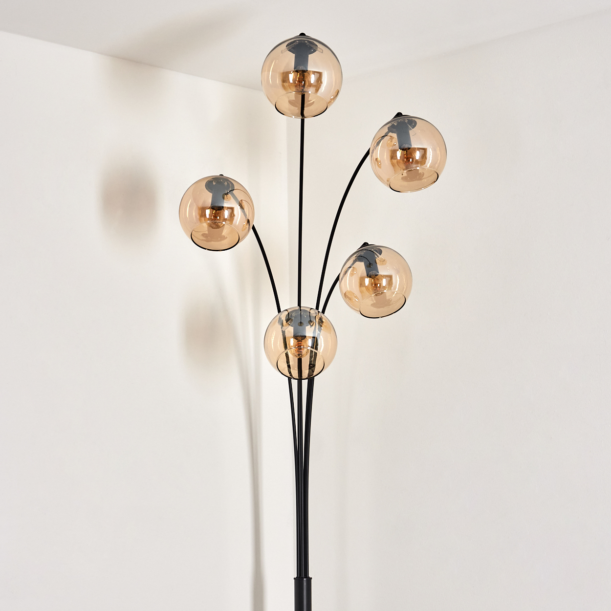 Stehlampe mit bernsteinfarbenen Glaskugeln vor einer weißen Wand.