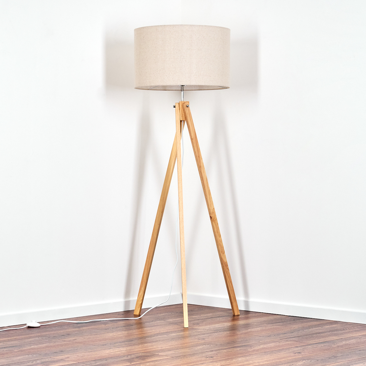 Eine hölzerne Stativ-Stehlampe mit beigem Lampenschirm steht in einer Ecke eines Raumes mit Holzboden.