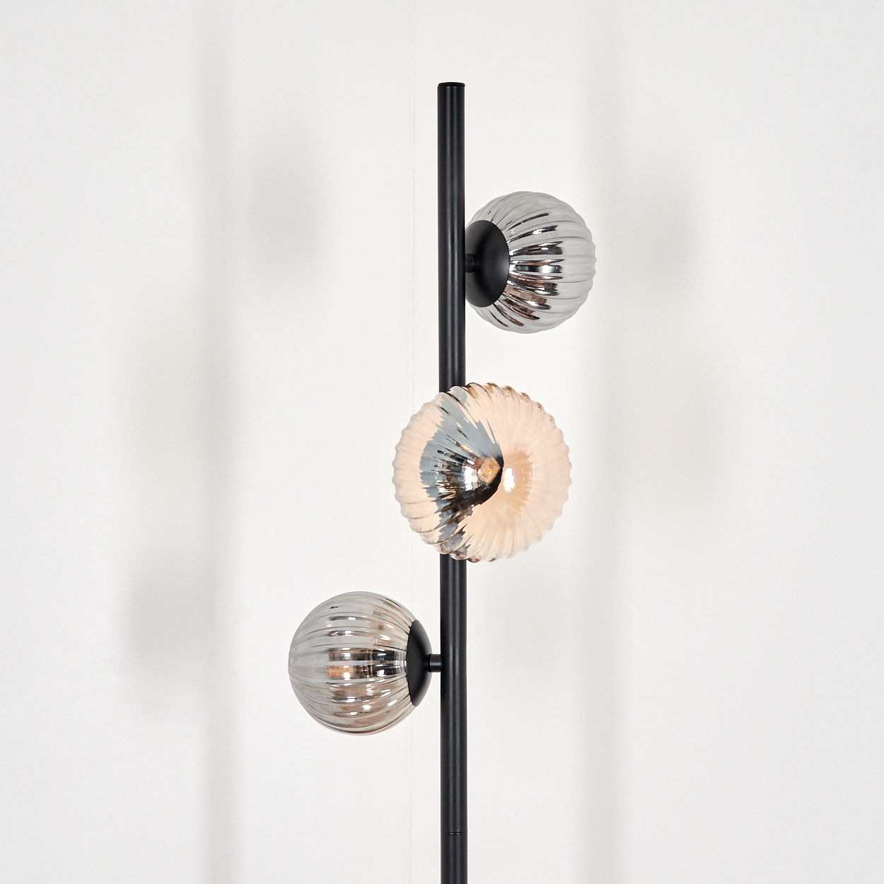 Schwarze Stehlampe mit drei Glasschirmen. Der Hintergrund ist weiß.