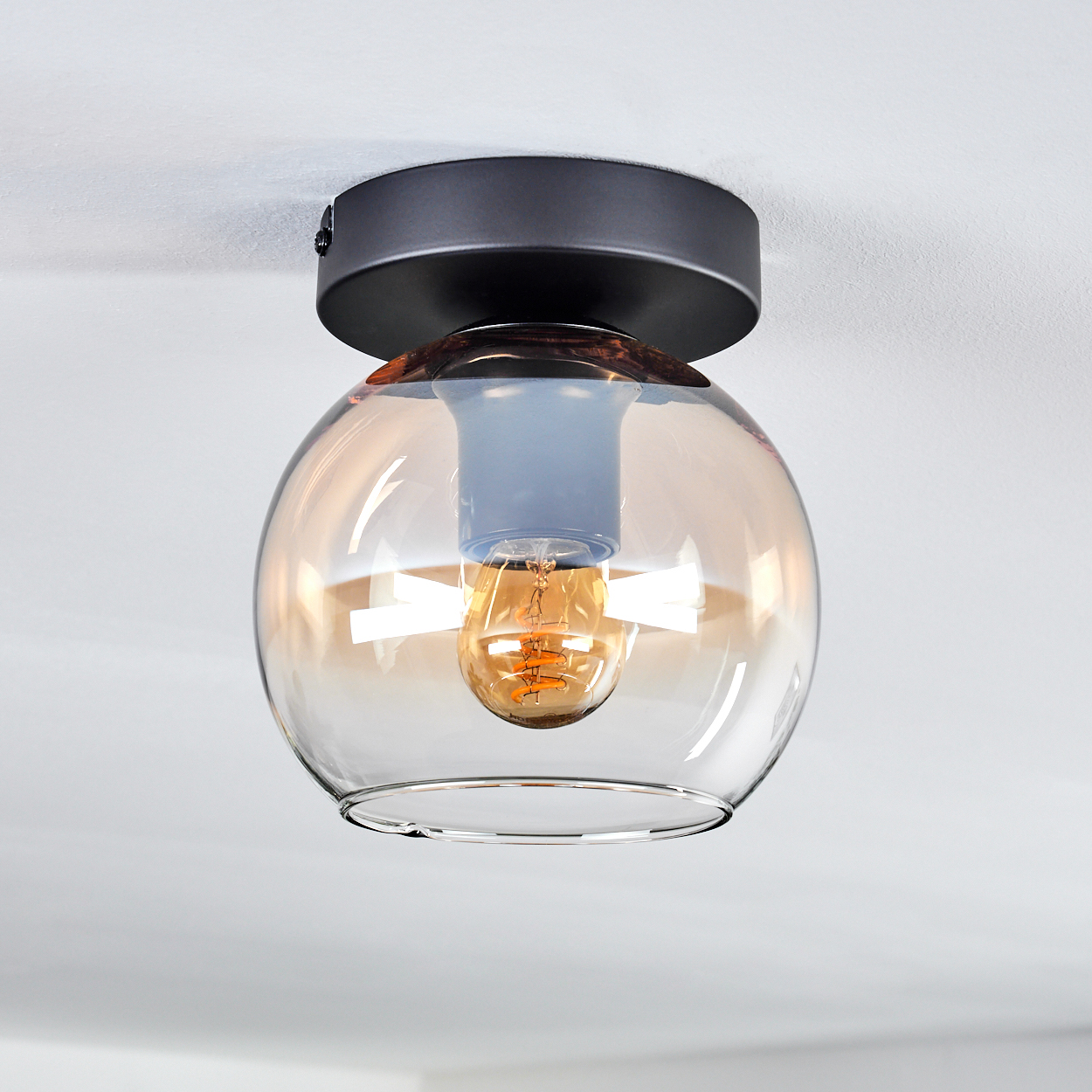Deckenlampe mit klarem Glaskugel und brauner Glühbirne. Der Hintergrund ist weiß.