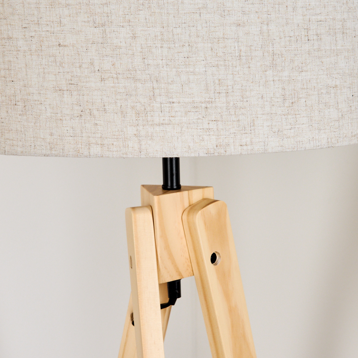 Dreibeinlampe aus Holz mit beigem Lampenschirm. Der Hintergrund ist schlicht.