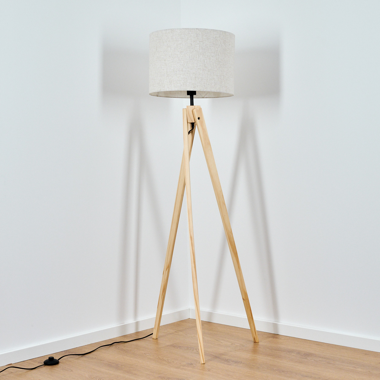 Holz-Stehlampe mit zylindrischem Lampenschirm in einer Ecke. Der Hintergrund ist weiß.