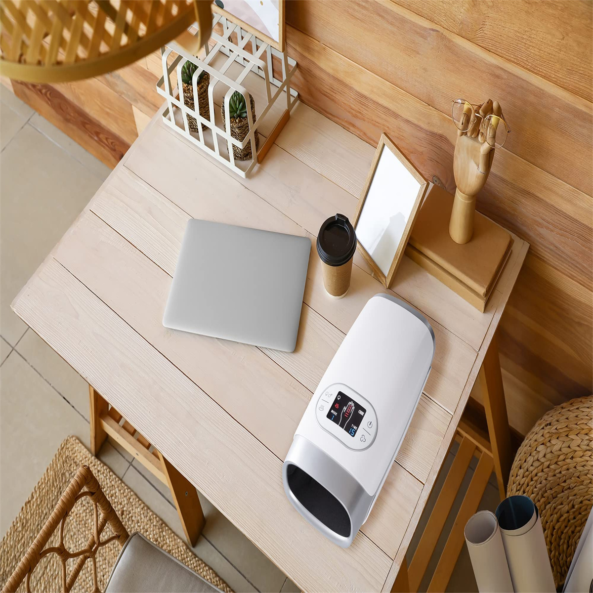 Ein Schreibtisch mit Laptop, Kaffeetasse, Handmassagegerät, Büchern und Dekoration. Der Tisch ist helles Holz.