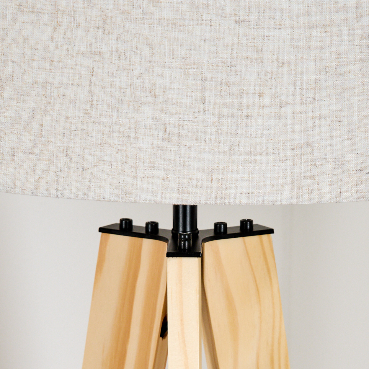 Nahaufnahme der Holzbeine eines Stativs und des hellen Lampenschirms einer Stehlampe.