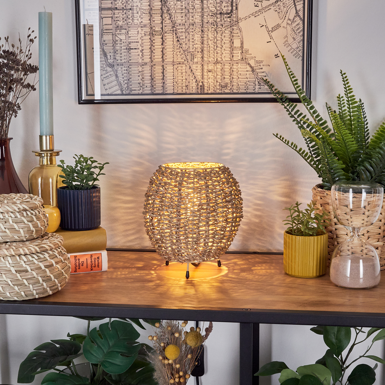 Innenszene mit beleuchteter gewebter Lampe, Pflanzen, Büchern und einer Karte auf Holzoberfläche.