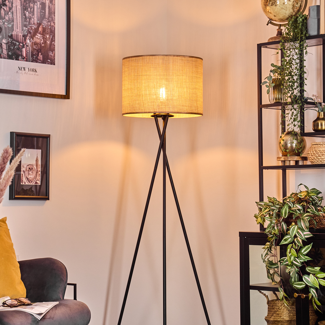 Eine beleuchtete Stehlampe mit beigem Schirm, in einem Raum mit einem New York-Poster und Pflanzen.