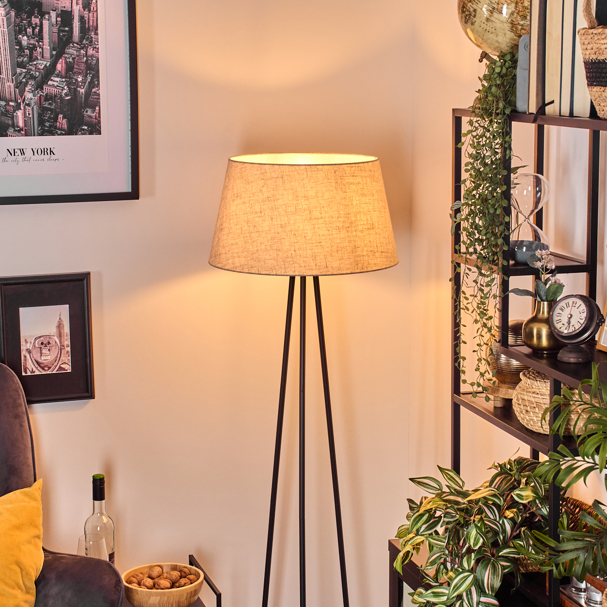 Stehlampe mit beigem Lampenschirm, schwarzen Beinen, in einem Wohnzimmer mit Bildern und Dekoration.