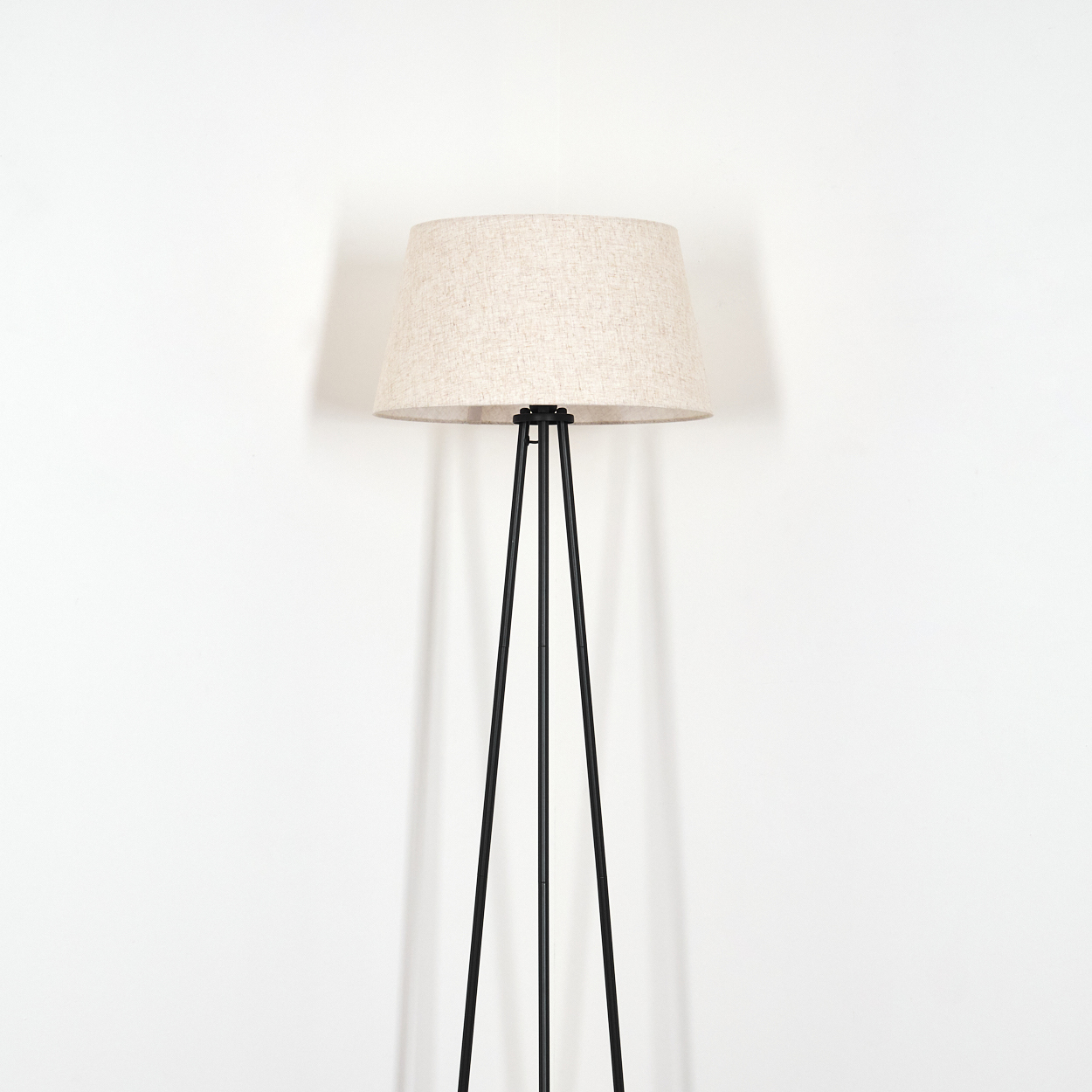 Stehlampe mit beigem Lampenschirm und schwarzem Rahmen vor weißem Hintergrund.