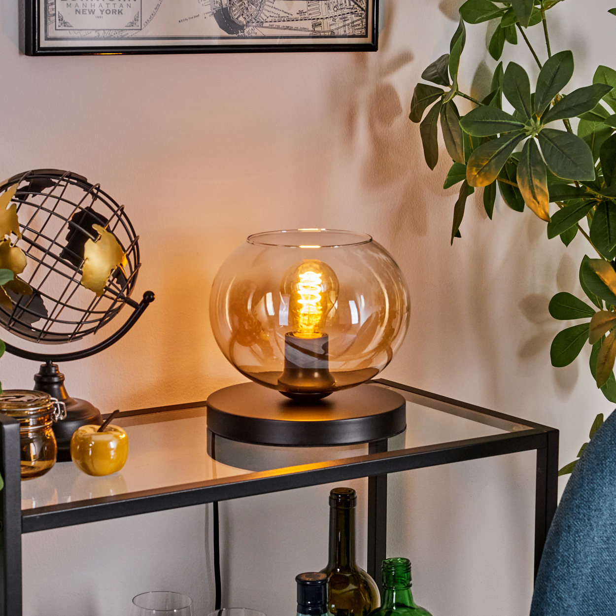 Eine kugelförmige Lampe mit Glasschirm steht auf einem Tisch mit Globus, Pflanze und Objekten.