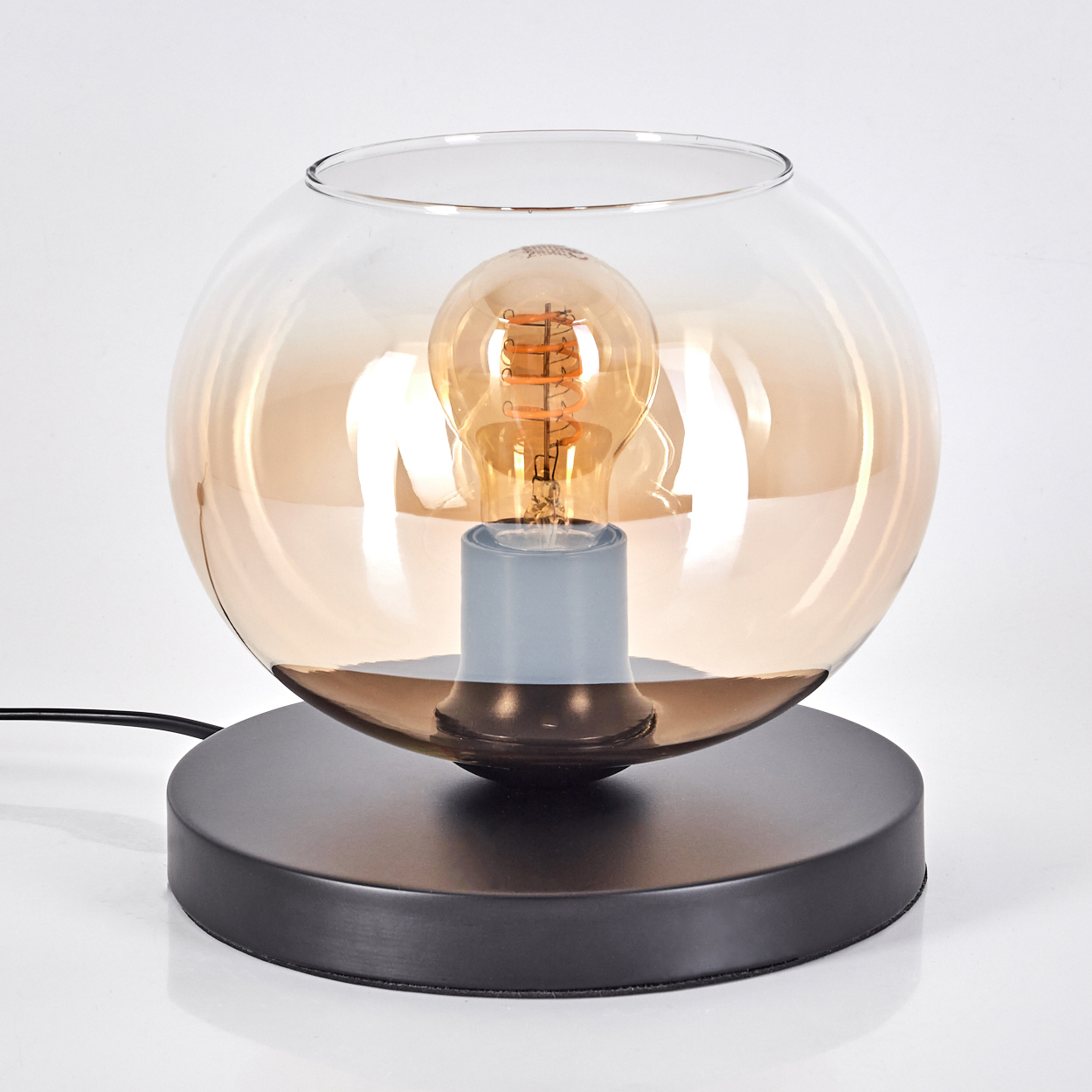 Eine runde Lampe mit Glasschirm und Edison-Glühbirne steht auf einem schwarzen Sockel.