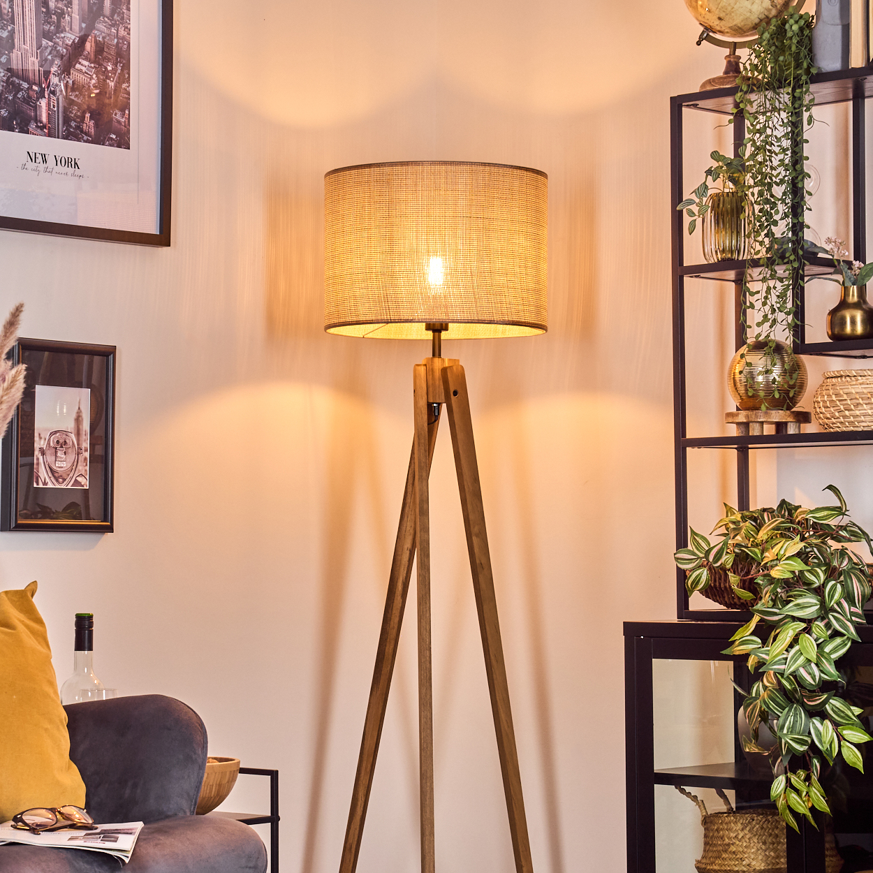 Stehlampe mit beigem Schirm, Holz-Dreibein-Fuß. Szene enthält Sessel und Deko.