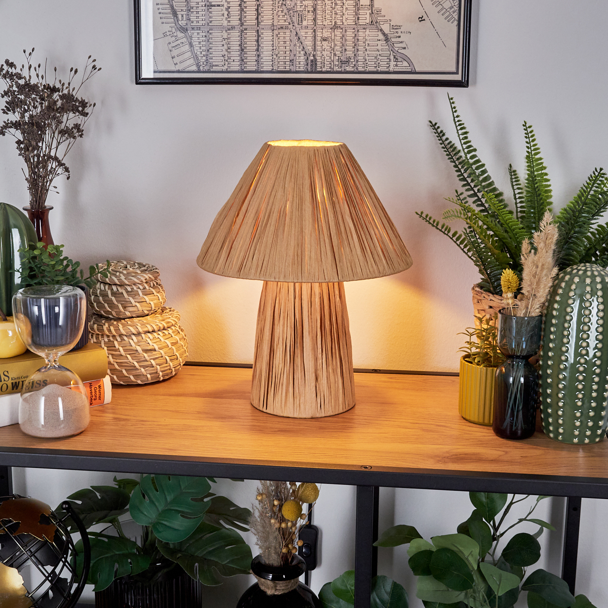 Eine Lampe mit pilzförmigem Lampenschirm auf einem Holztisch mit Dekoration. Hintergrund enthält Pflanzen und eine Karte.