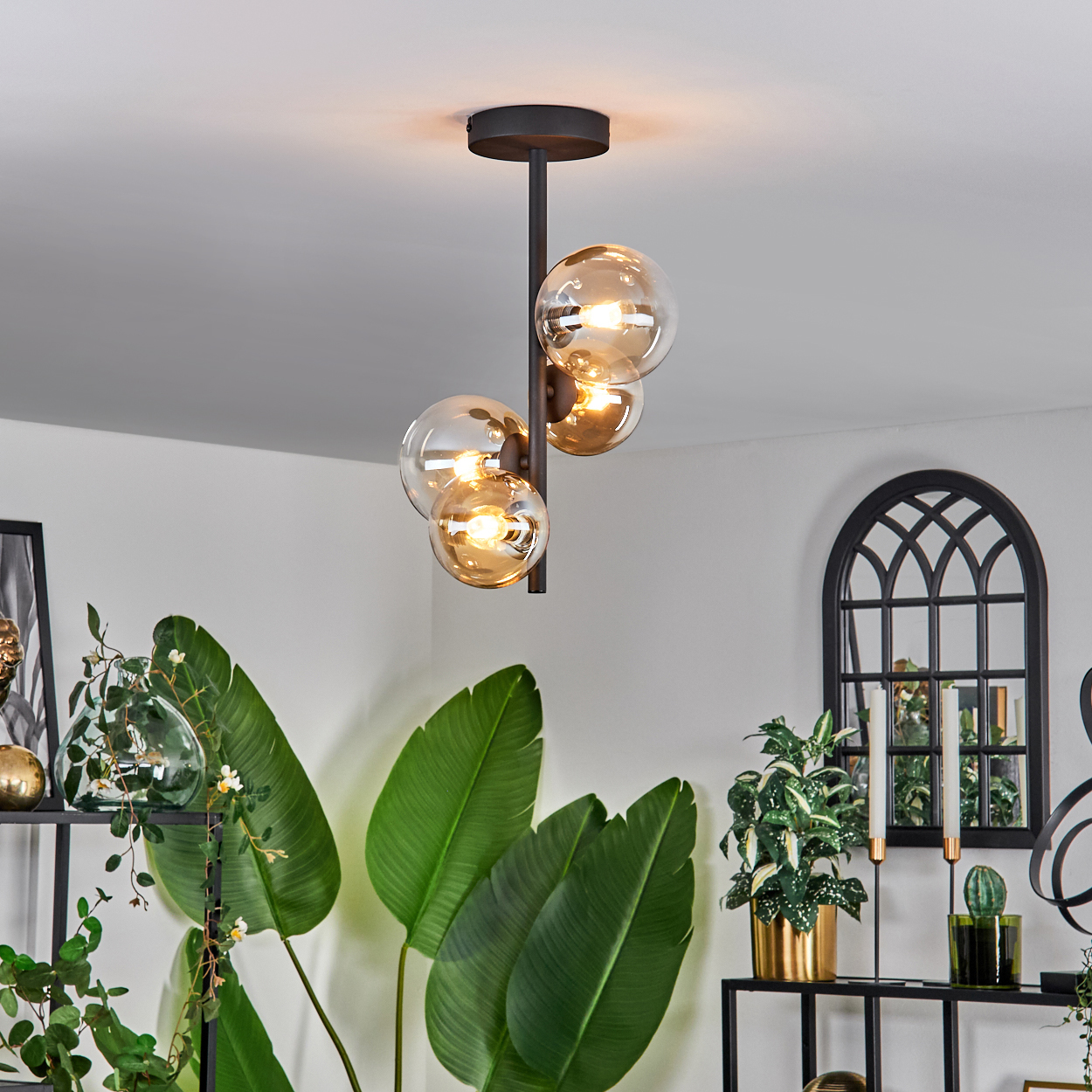 Deckenlampe mit drei bernsteinfarbenen Glaskugelleuchten. Innenraum mit Pflanzen und Dekorationen.